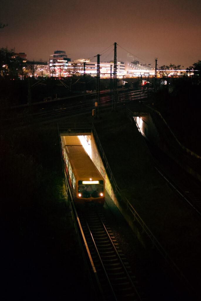 pociąg S-Bahn wyjeżdżający nocą z tunelu w Berlinie, w tle światła miasta